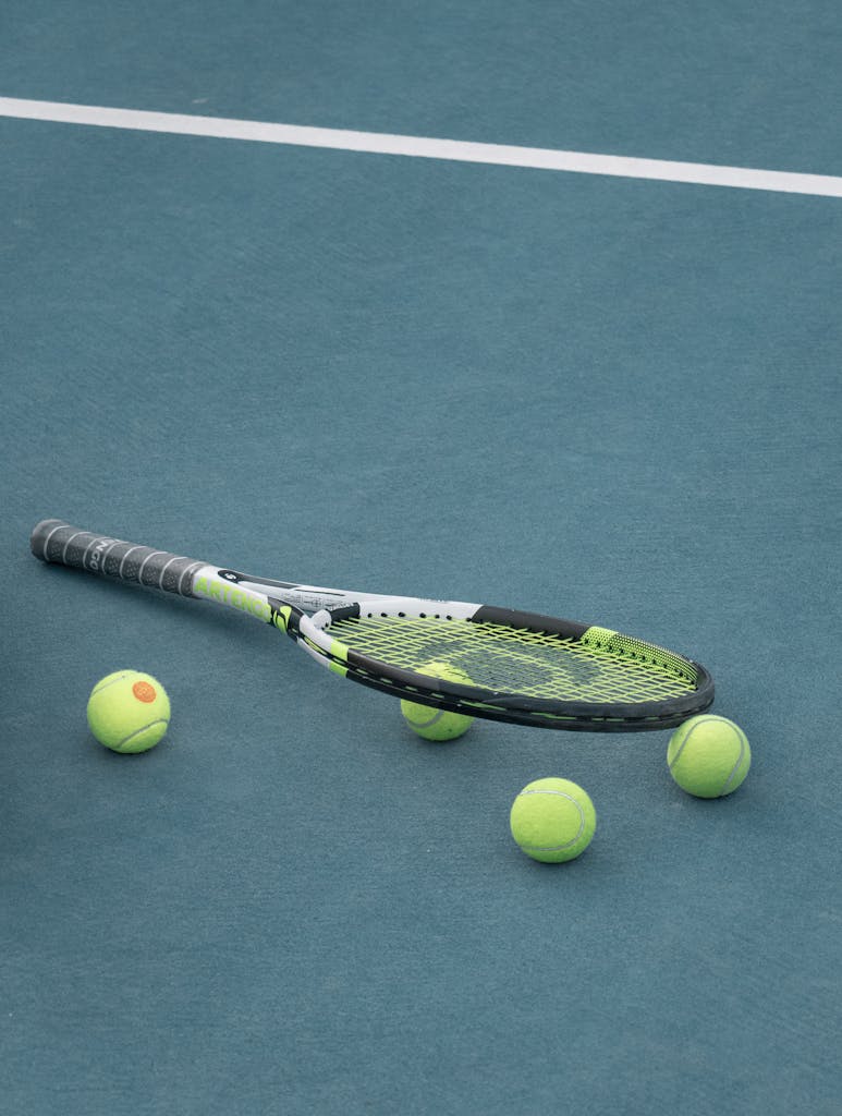 Tennis racket and balls on a blue court surface under day light.